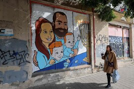 A woman walks past a mural paiting representing the Bibas family