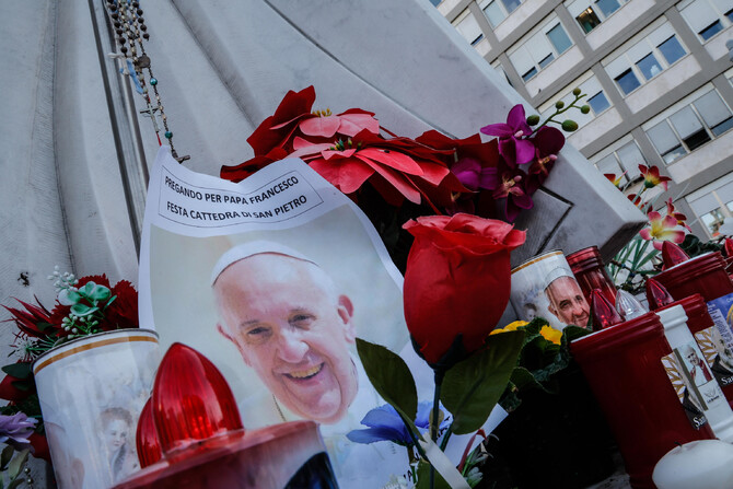 Candles with the pictures of Pope Francis are the laid under the statue of late Pope John Paul II